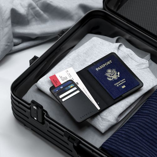 Ein schwarzer Reiseorganizer mit Reisepass, Tickets und Karten liegt in einem Koffer auf Kleidung.