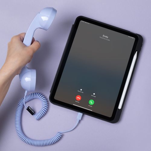 Una mano tiene una cornetta telefonica retrò azzurra collegata a un tablet che mostra una schermata di chiamata.