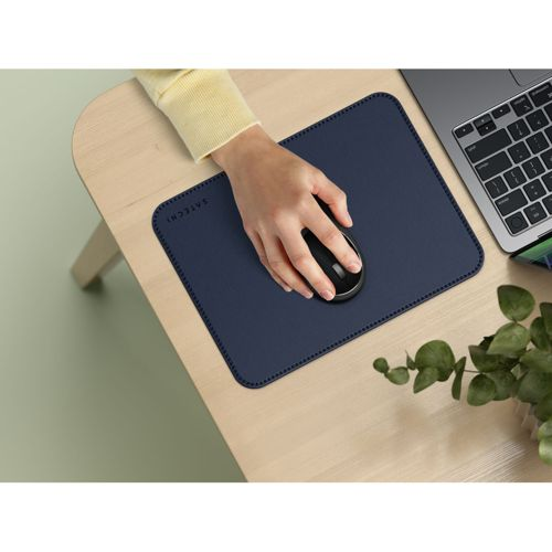 Eine Hand benutzt eine schwarze Maus auf einer blauen Unterlage neben einem Laptop.