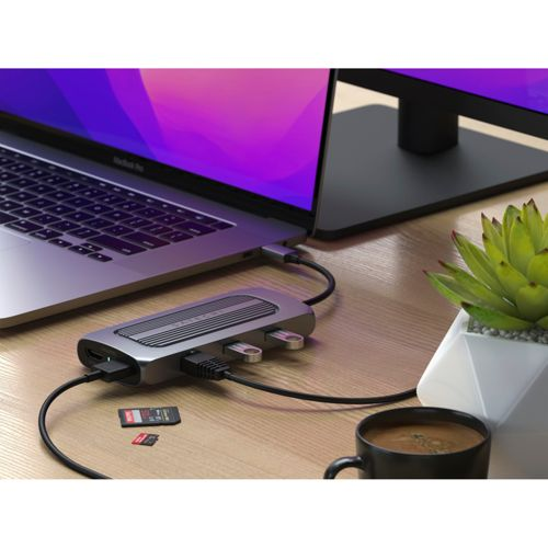Un hub USB argento collega un laptop a un monitor. Due schede SD sono vicine.