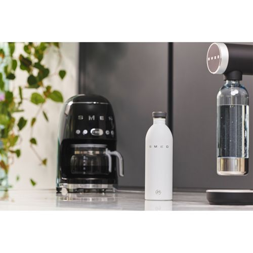 Eine schwarze SMEG-Kaffeemaschine steht neben einer weißen SMEG-Flasche und einem Wassersprudler.