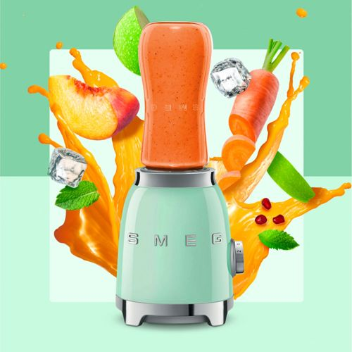 Ein mintgrüner Mixer mit Fruchtsaftspritzer, Pfirsich, Karotte, Limette und Eiswürfeln.