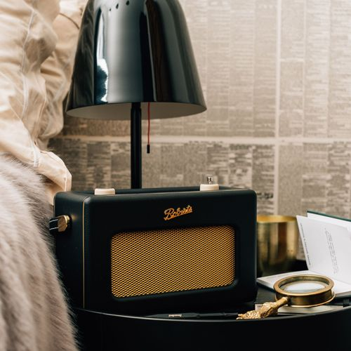 Een zwarte retro radio met goudkleurig rooster op een nachtkastje naast een lamp.