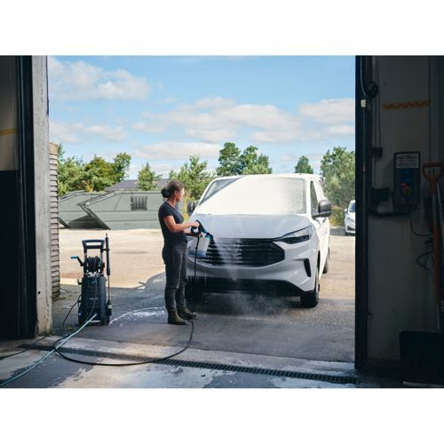 Una donna lava un furgone bianco con un'idropulitrice fuori da un garage.