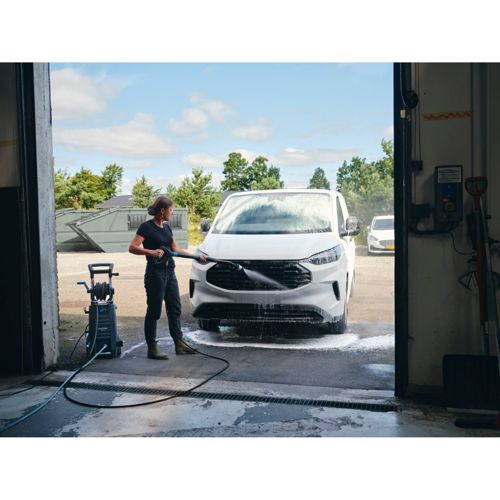 Donna lava furgone bianco con idropulitrice fuori dal garage al sole.