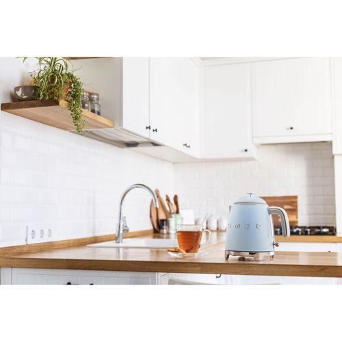 Een blauwe Smeg waterkoker staat op een houten aanrecht naast een kopje thee.
