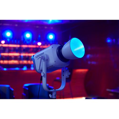 Een witte spotlight zendt blauw licht uit op een statief, met wazige blauwe en rode lichten op de achtergrond.