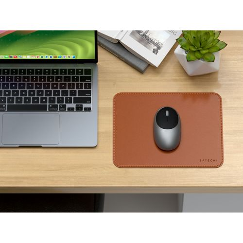 Ein Laptop, eine Maus auf einem braunen Mauspad, ein Buch und eine Pflanze.