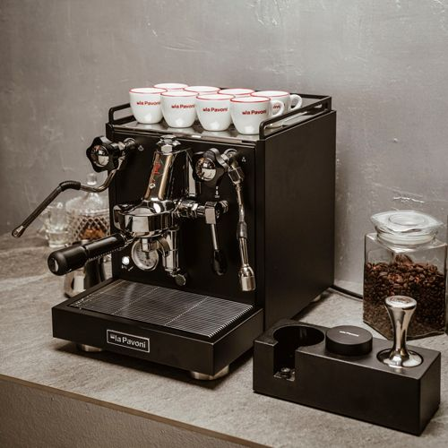 Una macchina per espresso nera con otto tazze e chicchi di caffè in un barattolo.