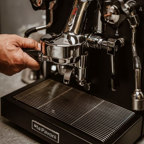 Una mano aziona una macchina da espresso nera con dettagli cromati e vassoio raccogligocce.