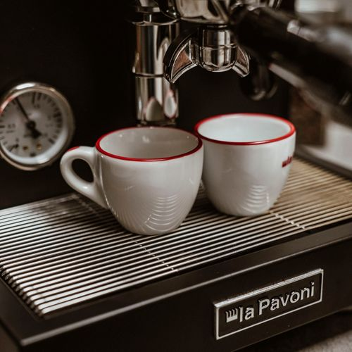 Due tazzine da espresso bianche con bordo rosso su macchina da espresso.