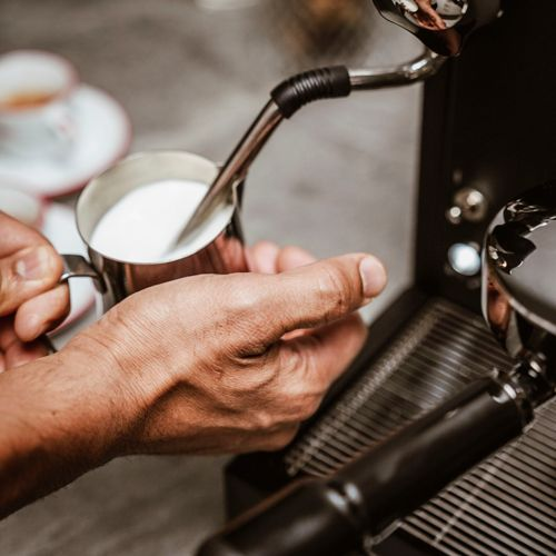 Una persona scalda il latte in una caraffa di metallo con una macchina per espresso.