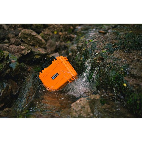 Eine orangefarbene wasserdichte Kiste liegt in einem Bach, umgeben von Felsen und Moos.