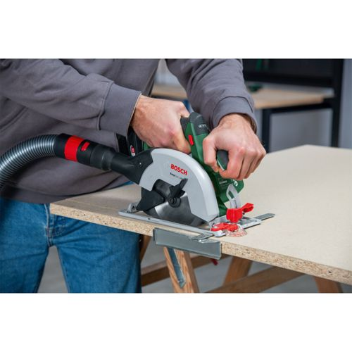 Ein Mann schneidet mit einer Bosch Kreissäge mit Absaugung Holz auf einem Tisch.