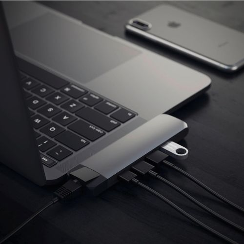 Laptop mit USB-Hub, Telefon und Kabeln auf dunkler Oberfläche.