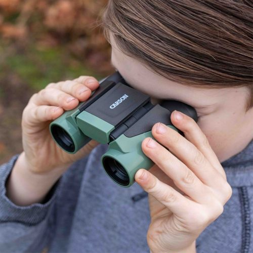 Una persona guarda attraverso un binocolo verde e nero in un ambiente boscoso.