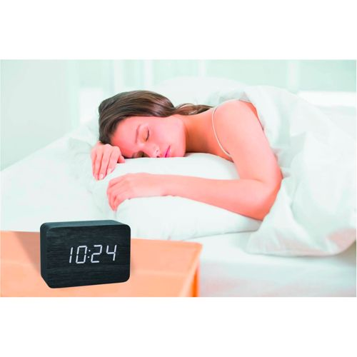 Eine Frau schläft im Bett neben einem schwarzen Digitalwecker, der 10:24 anzeigt.