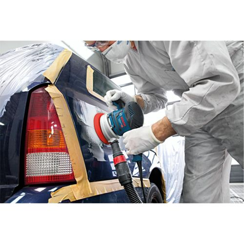 Mann mit Schutzmaske poliert Auto mit blauem Schleifgerät.