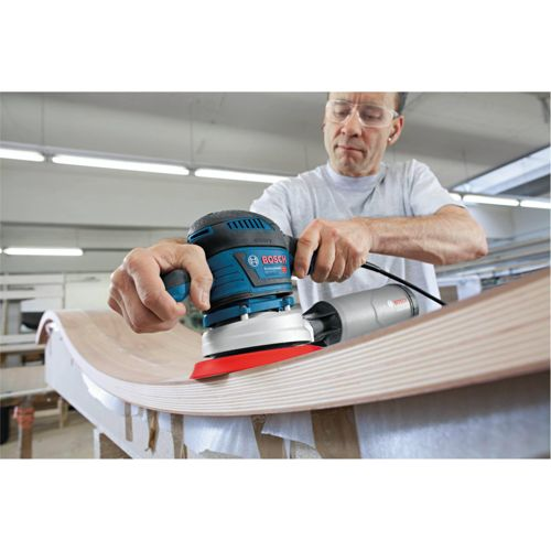 Mann schleift Holzoberfläche mit blauer Bosch-Schleifmaschine.