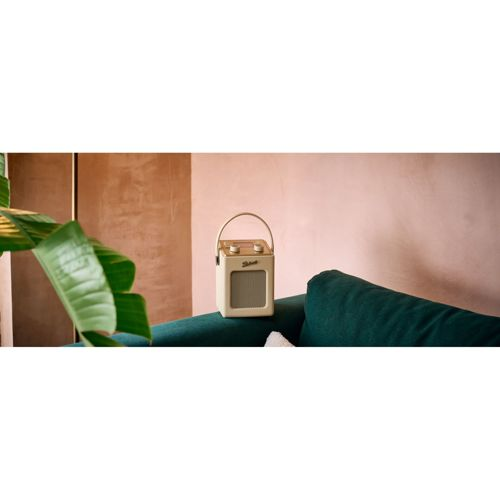 Une enceinte rétro de couleur crème est posée sur un canapé vert devant un mur rose.