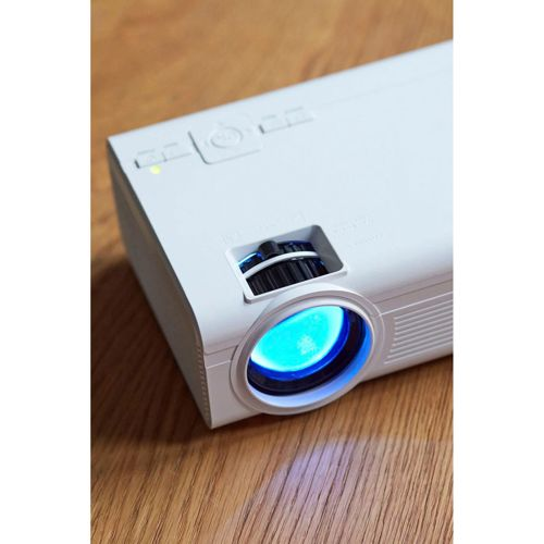Ein weißer Projektor mit blauem Licht leuchtet auf einem Holztisch.