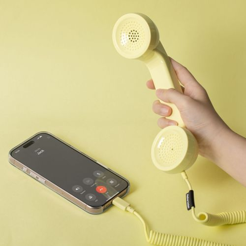 Una mano tiene una cornetta gialla collegata a un iPhone. Sfondo giallo.