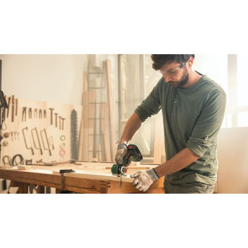 Mann mit Schutzbrille und Handschuhen benutzt einen Bohrer in einer Werkstatt.