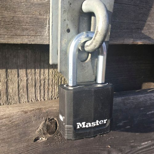 Ein schwarzes Vorhängeschloss von Master mit silbernem Bügel, das an einer Holztür befestigt ist.