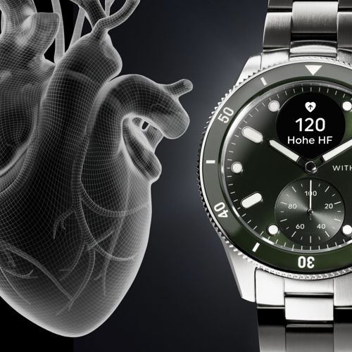 Drahtgitter-Herz neben einer grünen Smartwatch mit Herzfrequenzanzeige.