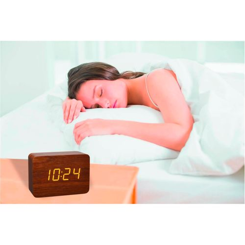 Eine Frau schläft im Bett neben einer hölzernen Digitaluhr, die 10:24 anzeigt.