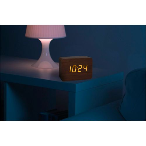 Holzwecker zeigt 10:24 neben einer Lampe auf einem Nachttisch.