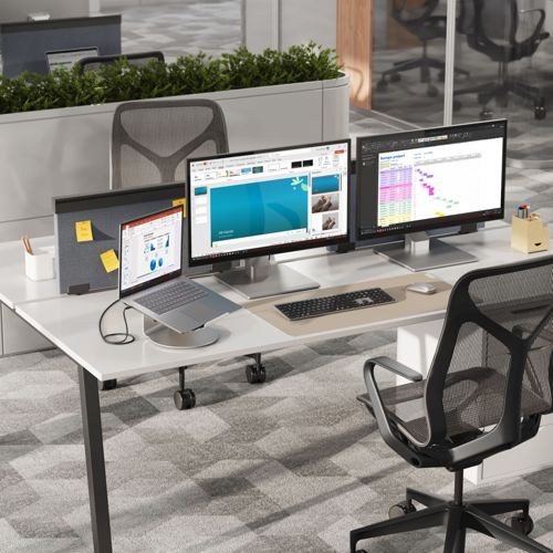 Ein moderner Schreibtisch mit drei Monitoren, einem Laptop und einem Bürostuhl.