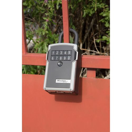 Una caja de seguridad con candado de combinación gris y detalles plateados, sujeta a una puerta roja.