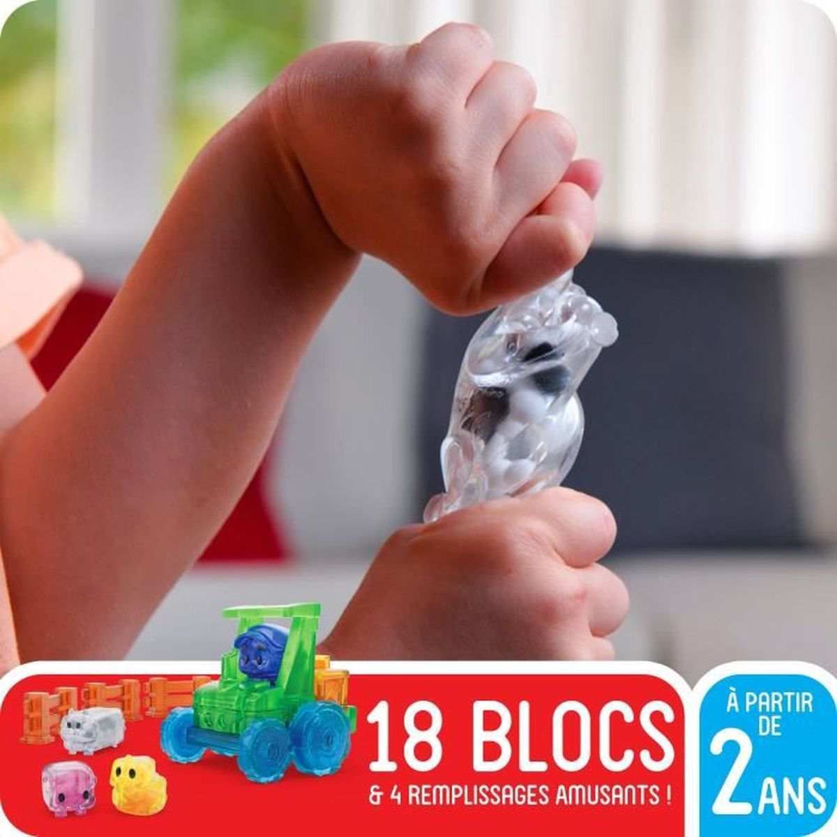 Bambino tiene figura trasparente con palline. Trattore giocattolo e blocchi in primo piano.