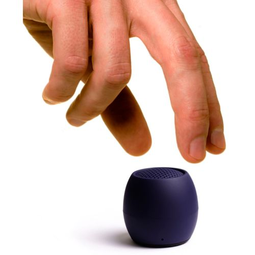 Een hand reikt naar een kleine, donkerblauwe, bolvormige luidspreker met een geperforeerde bovenkant op een witte achtergrond.