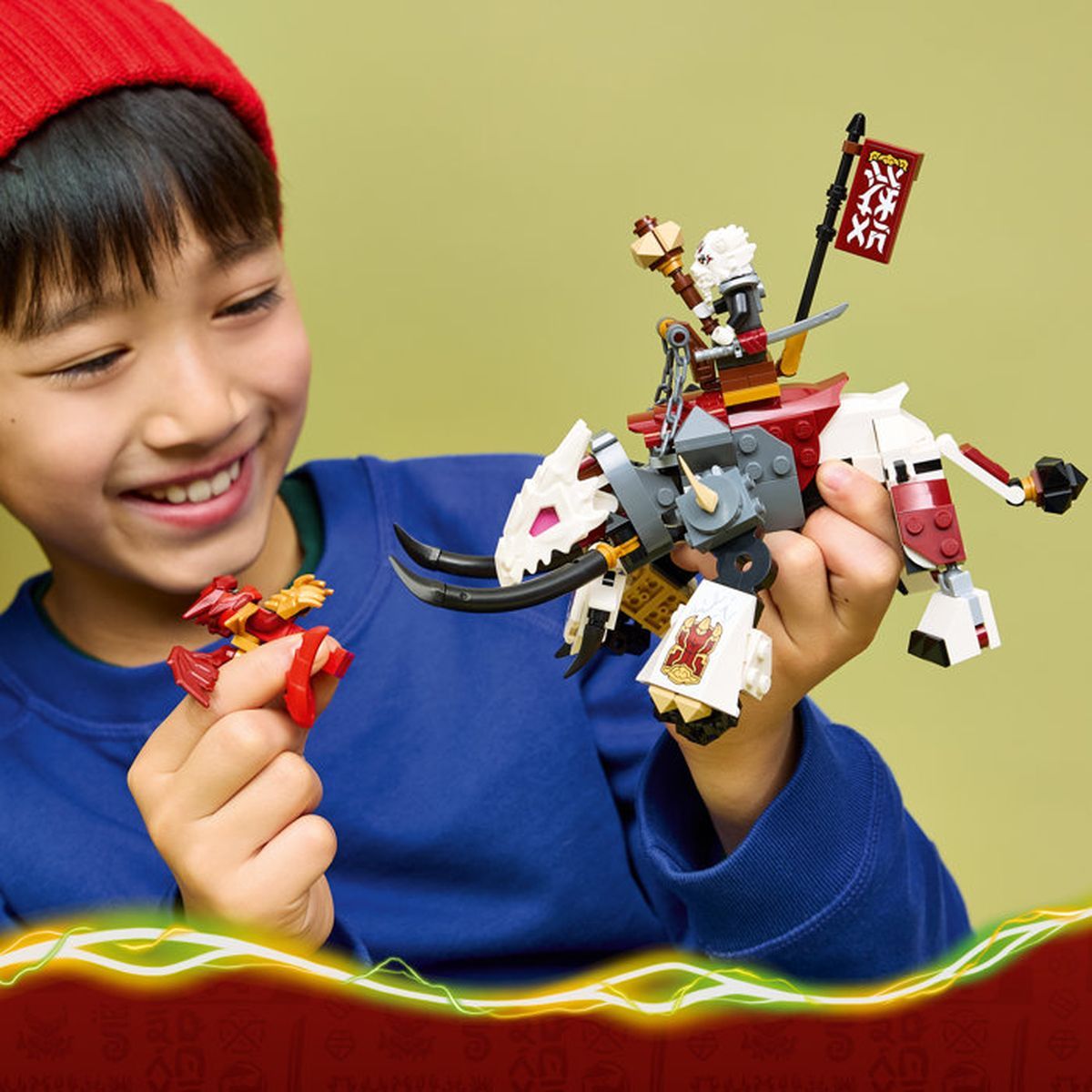 Un ragazzo con cappello rosso tiene un giocattolo drago Lego con cavaliere e un drago rosso più piccolo.