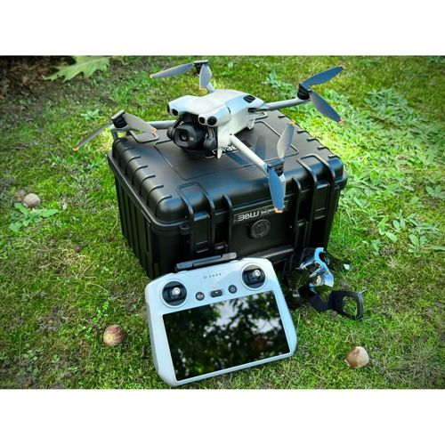Un drone riposa su una custodia nera, con un controller nelle vicinanze sull'erba.