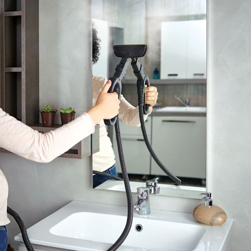 Pulitore a vapore pulisce specchio sopra lavabo, mani che tengono il dispositivo.