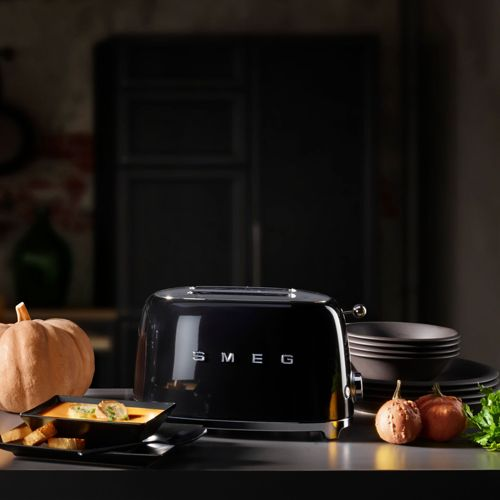 Ein schwarzer Toaster steht auf einer Arbeitsplatte neben einem Kürbis und einer Schüssel Suppe.