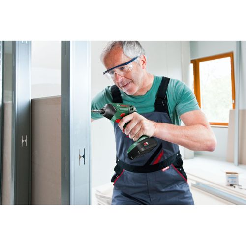 Mann in Blaumann und Schutzbrille benutzt Akkuschrauber an Metallrahmen.