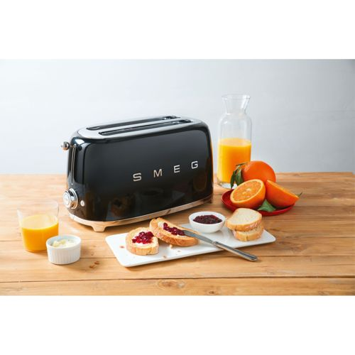Siyah Smeg tost makinesi, ahşap masa üzerinde kızarmış ekmek, reçel, tereyağı, portakal ve meyve suyu.