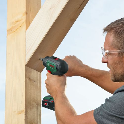 Mann schraubt mit Akkuschrauber Holzkonstruktion zusammen, Schutzbrille trägt er.