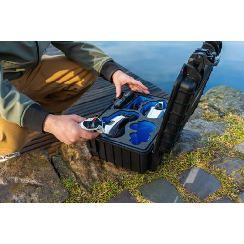 Persona tiene controller vicino a valigetta nera aperta con droni bianchi e inserti in schiuma blu.