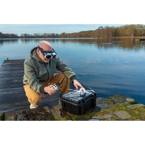 Uomo con occhiali VR e controller drone vicino a un lago.