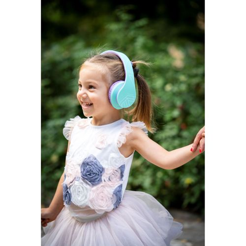 Una bambina sorridente con cuffie turchesi e vestito floreale all'aperto.