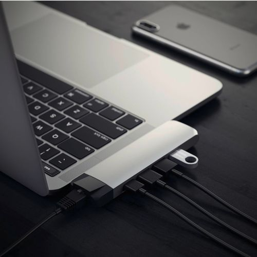 Silberner Laptop mit USB-Hub, Kabeln und Telefon auf dunkler Oberfläche.