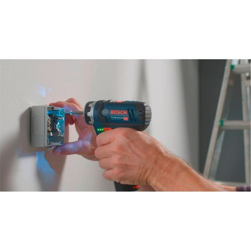 Une personne utilise une perceuse Bosch pour visser dans une boîte de prise murale. Une échelle est visible à l'arrière-plan.