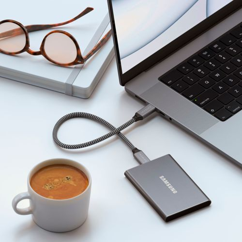 Un SSD Samsung collegato a un laptop, con caffè e occhiali nelle vicinanze.