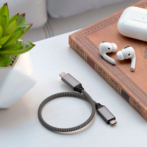 Un cavo USB-C grigio con due connettori giace accanto a un libro e auricolari wireless.