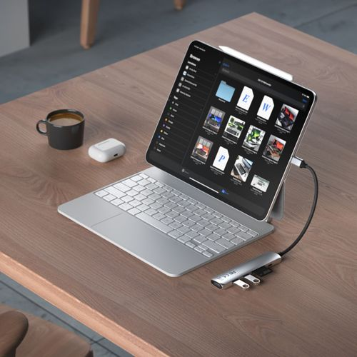 Un tablet argento con tastiera, stilo, auricolari e tazza caffè su tavolo legno.